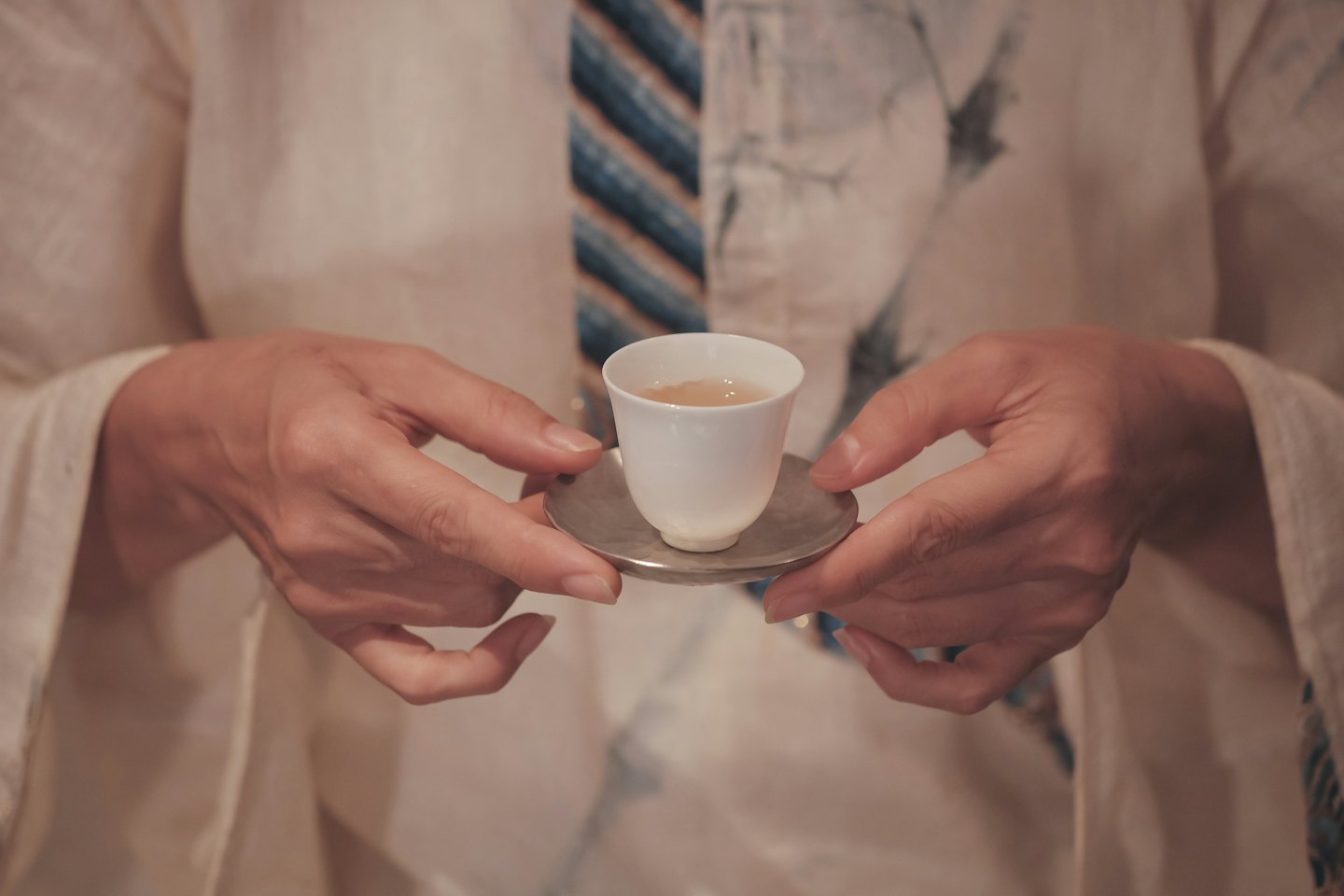 Hände halten eine zarte weiße Teetasse, gefüllt mit Tee.